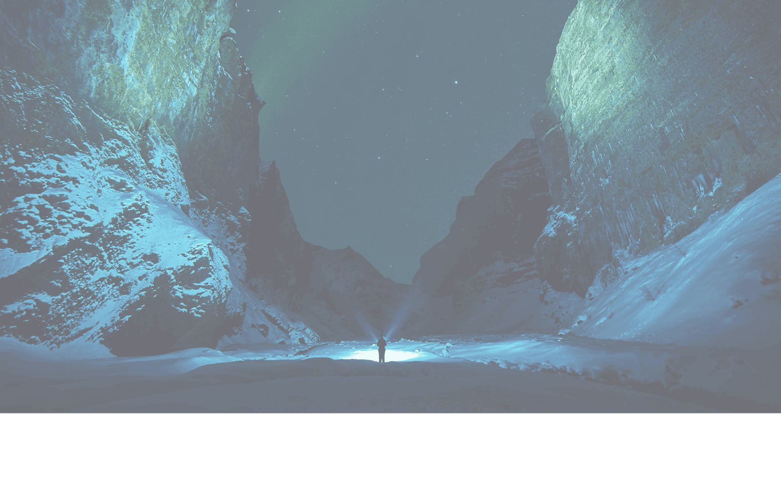 A person stands in a cave, illuminated by a bright light, highlighting the cave's rocky textures and shadows.